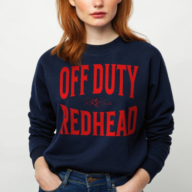 A redhead wears a classic navy blue relaxed fit unisex sweatshirt with the words 'OFF DUTY REDHEAD' written in large Brookfield red font, across the front. Branded RedBlonde London in red on inside neck and right sleeve