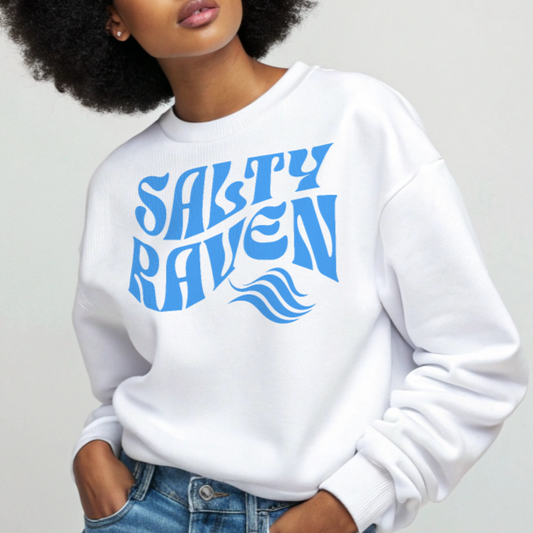 Afro woman wears aClassic relaxed fit unisex sweatshirt in white with 'Salty Raven' play on words slogan in blue retro wavy 70s text. Branded RedBlonde on inside neck and right cuff in red