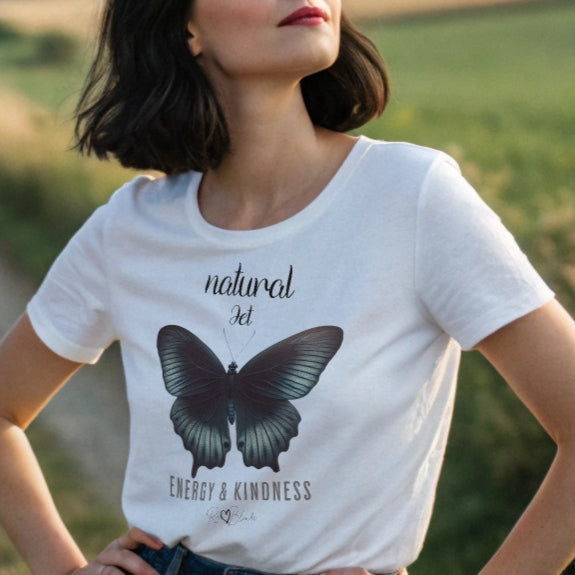 Black haired woman wears white unisex relaxed fit t-shirt with the words natural Jet in arionna font above a graphic of a black butterfly with 'ENERGY & KINDNESS' below in adventurer 06 font signed off by RedBlonde.