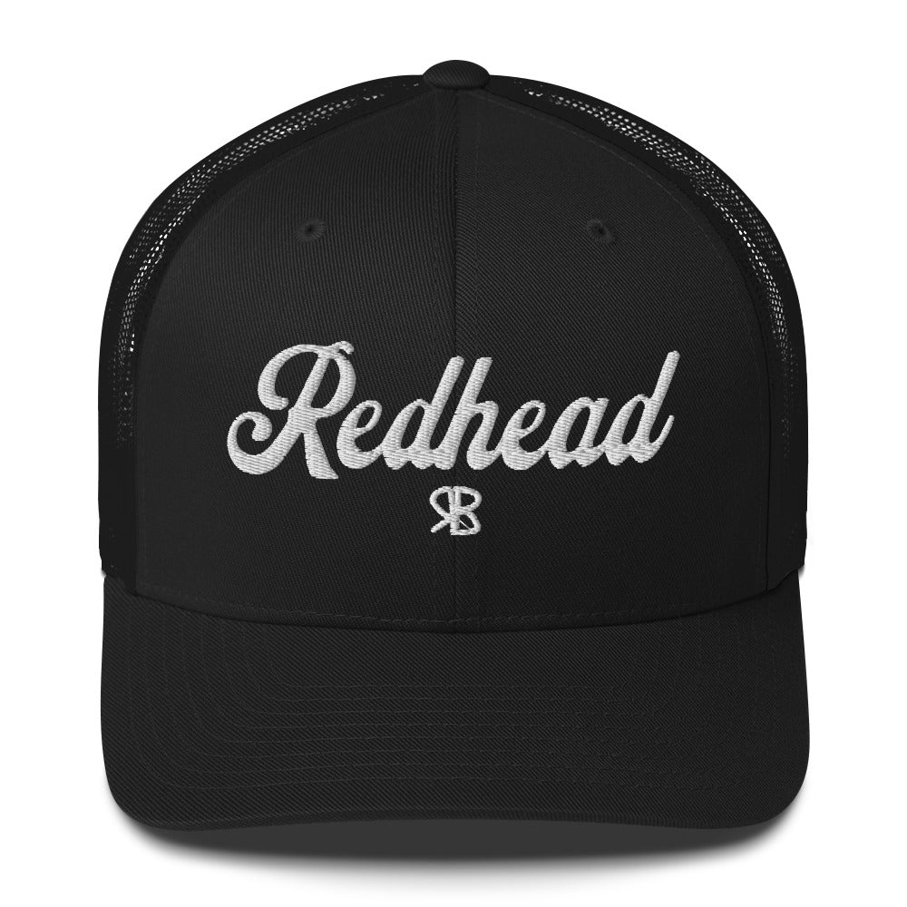 Black trucker cap with 'Redhead' in white adventurer 01 font on front. Mesh back. Branded RB