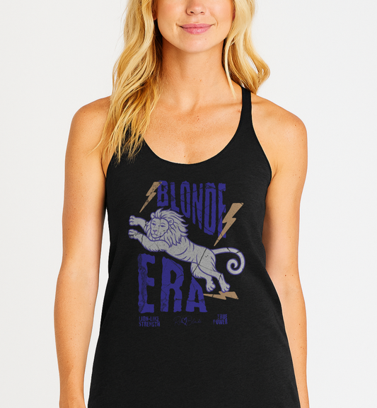 Blonde woman wears a women’s vintage-style racerback tank in heathered black features a large, stylized illustration of a lion leaping forward in pale purple and white with a flowing mane. Bold, distressed text above and below reads “BLONDE ERA” in uppercase purple letters, with two orange lightning bolts flanking the text. Beneath the lion in small purple letters are the phrases “Lion-like strength” and “True power.” RedBlonde with a heart small signature-like logo appears below the text.