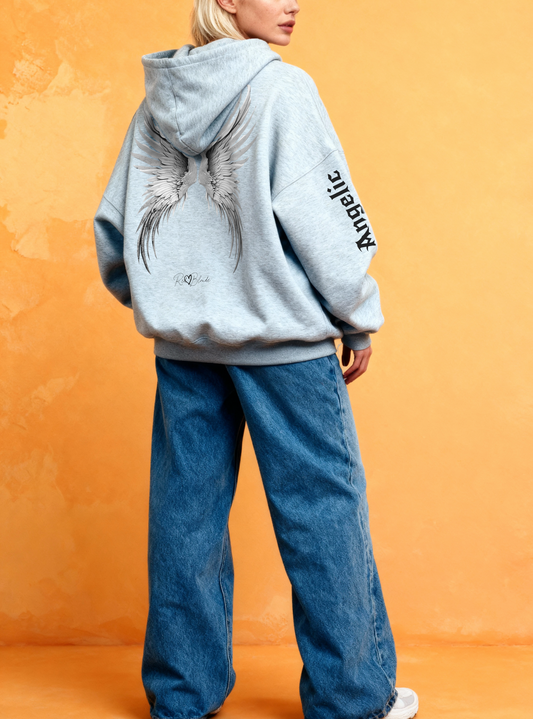 Back view of a blonde wearing a light grey hoodie featuring large silver angel wings printed across the back, with black RedBlonde signature logo underneath. Each sleeve features gothic New Rockstar font graphic text one sleeve says 'Angelic' and the other 'Blonde'