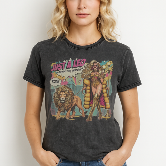 Blonde wears a unisex black denim wash vintage t-shirt with a retro pop-art Leo graphic featuring a long curly haired blonde woman in a gold swimsuit, gold over the knee boots, gold medallion and long fur coat, walking a lion on a leash wearing a gold medallion, with a caption bubble 'Roar', with a city and round bulb street lights in the background captioned ‘Just a Leo, Owning the Spotlight'. Branded RedBlonde on inside neck and right shoulder