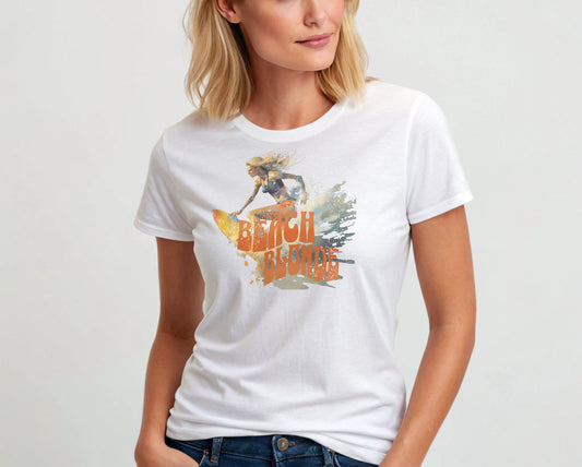 Blonde wears a white unisex relaxed fit t-shirt featuring a graphic of a blonde woman surfing with waves splashing around her and the words "BEACH BLONDE" in bold orange Solino Display font. Branded RedBlonde London on the inside neck and right sleeve