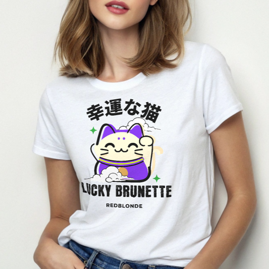Brunette wears A white unisex T-shirt with a classic crew neckline and short sleeves. The front features a colorful graphic of a waving Maneki-neko (lucky cat) in cream and purple, surrounded by small green sparkles. Above the cat, bold black Japanese characters are displayed. Below the cat, the text reads “LUCKY BRUNETTE” in black block letters, with “REDBLONDE” printed underneath in smaller font. Branded RedBlonde in red inside neck and right sleeve