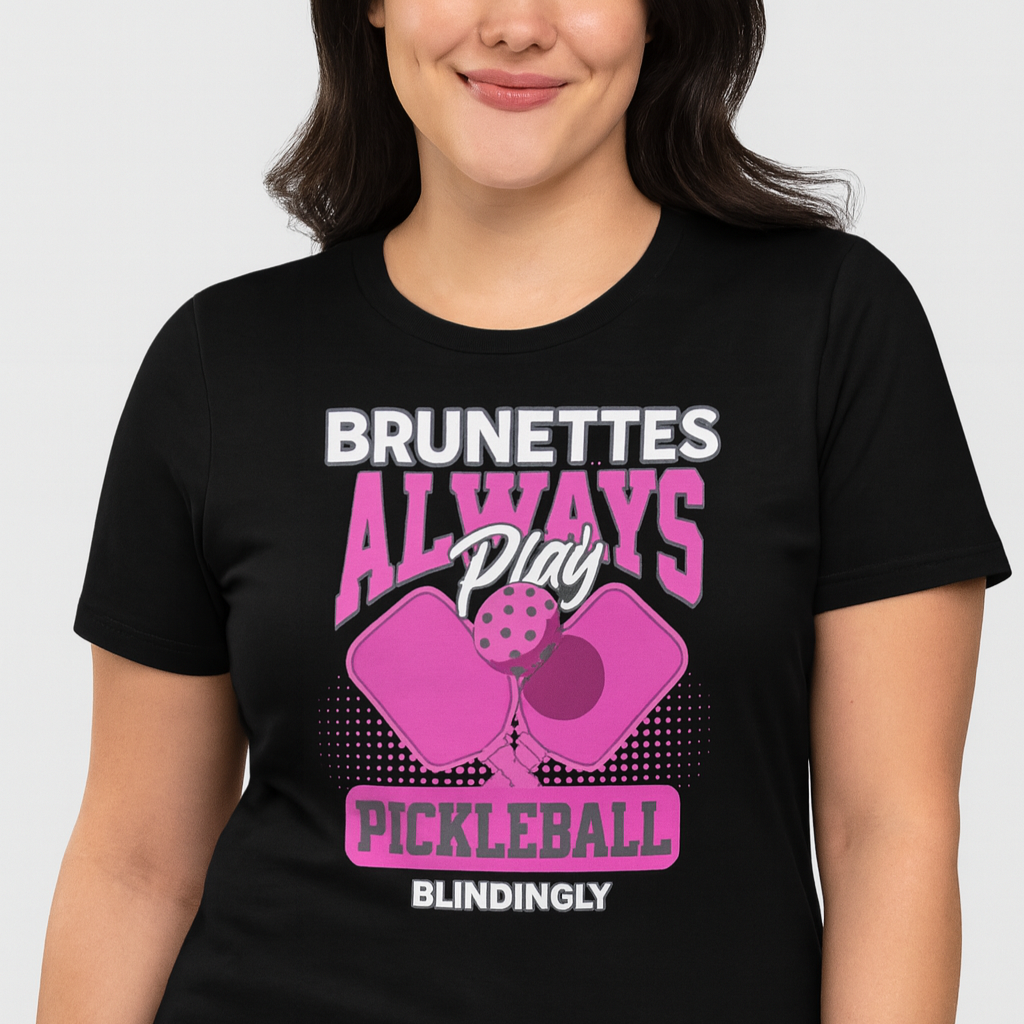 Brunette wears a Black unisex t-shirt with bold pink and white graphic that says "Brunettes Always Play Pickleball Blindingly," featuring two pink pickleball paddles and a ball. Branded RedBlonde on inside neck and right sleeve