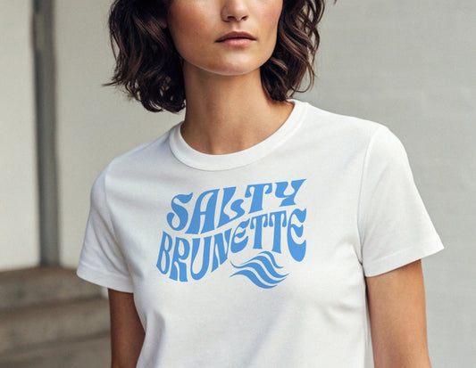 Brunette wears a white classic unisex graphic t-shirt with the slogan 'Salty Brunette' in Solino Display blue retro 70s wavy font. Branded RedBlonde in red on inside neck and right sleeve