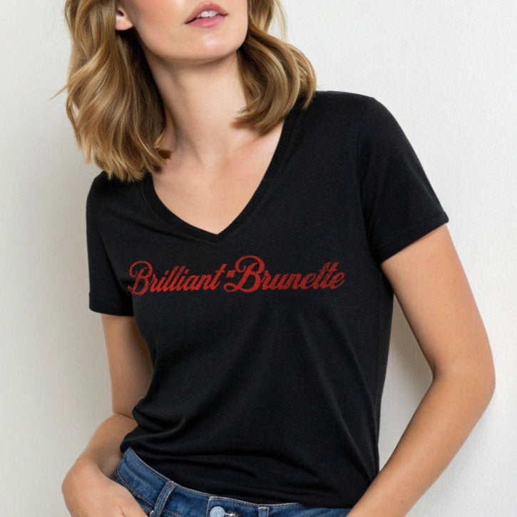 Brunette wears black women's relaxed fit v-neck slogan t-shirt with 'Brilliant Brunette' in milkshake script red font. Branded RedBlonde in red on inside neck and right sleeve