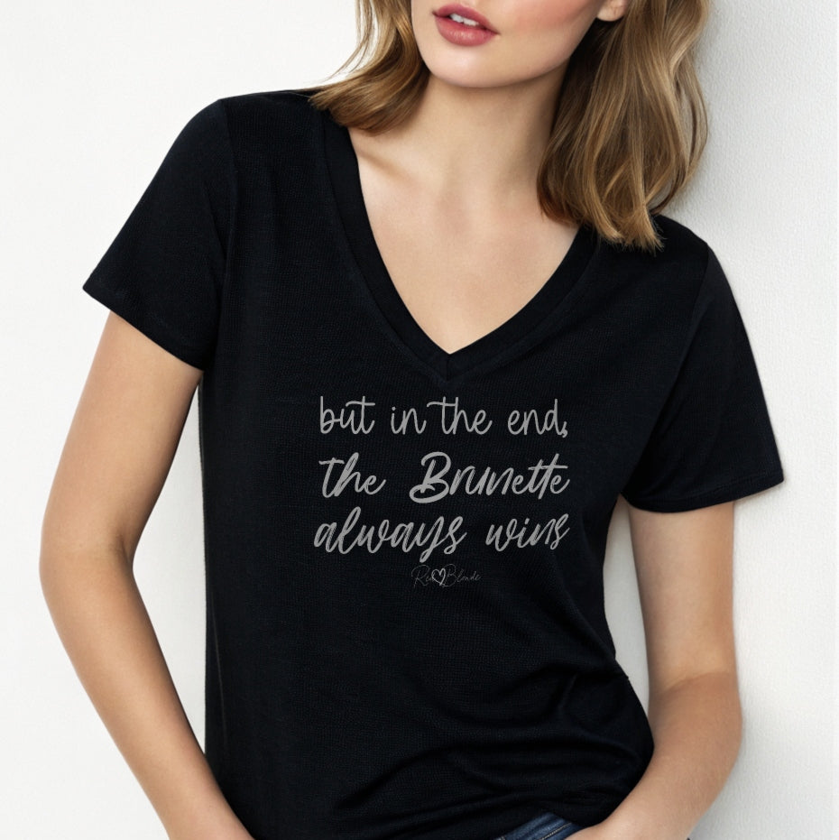 Brunette woman wears a black women's v-neck relaxed fit t-shirt featuring the handwritten-style slogan “but in the end, the Brunette always wins” in Hillbear font in light gray text across the chest, signed off RedBlonde. Branded “RedBlonde London on inside the collar and on the right sleeve