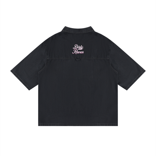 Back view of a black, short-sleeve button-up shirt with a subtle faded finish and a small raised “Dirty Raven” Milkstore script logo centered across the upper back.