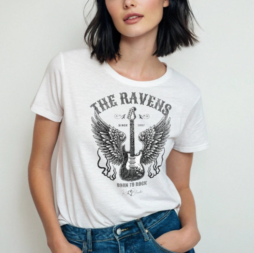 Girl with black hair wears a white unisex t-shirt with a graphic of a black & white guitar with raven bird wings emerging from the side. The graphic features ‘THE RAVENS’ in Sancreek font in a semicircle above the guitar, while ‘BORN TO ROCK’ is underneath. Branded RedBlonde London in inside neck and right sleeve