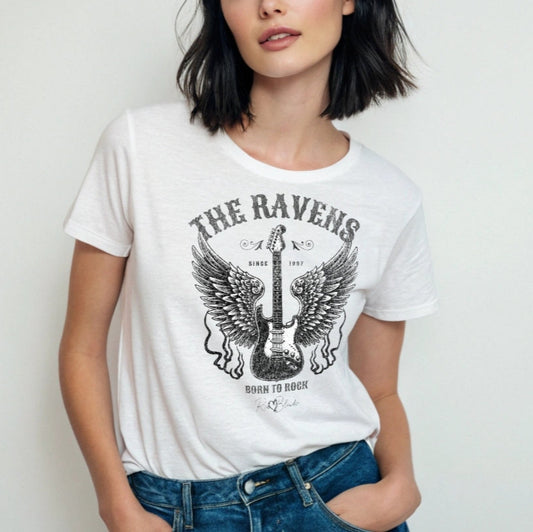 Girl with black hair wears a white unisex t-shirt with a graphic of a black & white guitar with raven bird wings emerging from the side. The graphic features ‘THE RAVENS’ in Sancreek font in a semicircle above the guitar, while ‘BORN TO ROCK’ is underneath. Branded RedBlonde London in inside neck and right sleeve