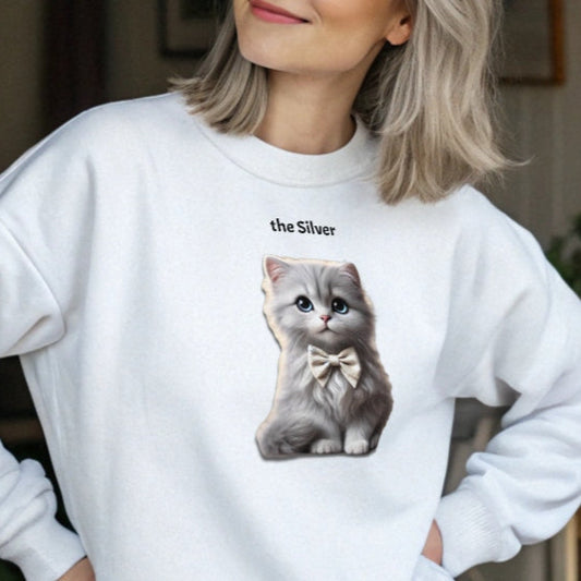Grey haired model wears white relaxed fit unisex sweatshirt with a cute graphic of a silver kitten wearing a bow-tie and the words 'the Silver' linking to silver hair. Branded RedBlonde in red on inside neck and right cuff