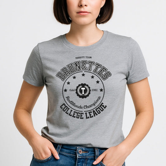Light grey unisex t-shirt featuring a bold black collegiate-style graphic that reads "BRUNETTES COLLEGE LEAGUE" with stars and a central crest emblem. The design includes "Varsity Team," "RedBlonde Champions," and "Estd 1981" details. RedBlonde branding appears on the inner neck label and left sleeve in red text.