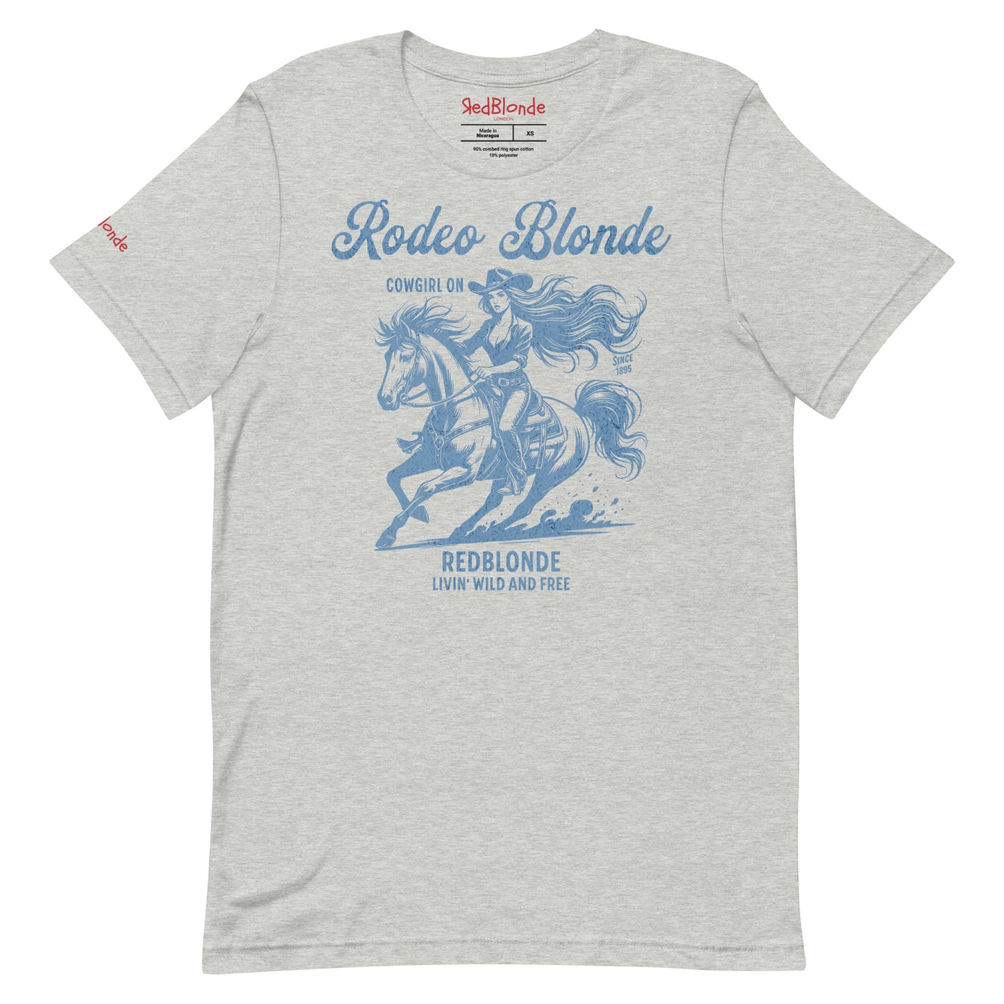 Light grey unisex t-shirt featuring a vintage-style western graphic in soft blue. The design shows a long-haired cowgirl in motion riding a galloping horse, wearing a wide-brimmed hat. Above the image, the text reads "Rodeo Blonde" and "Cowgirl On," while below it says "REDBLONDE – Livin' Wild and Free." RedBlonde branding appears on the inner neck label and right sleeve in red text.