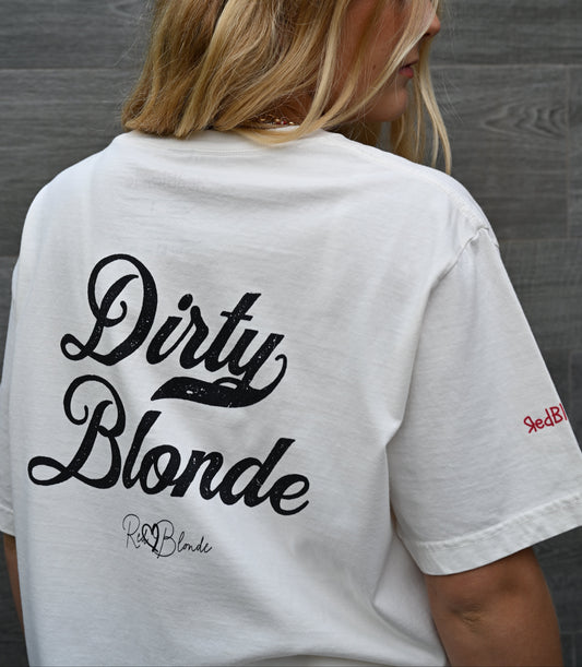 Back view of a blonde wearing a light blue washed oversized unisex T-shirt with bold black Milkstore 01 vintage-style script reading “Dirty Blonde” and the RedBlonde signature logo beneath, plus a small RedBlonde logo detail on the right sleeve.
