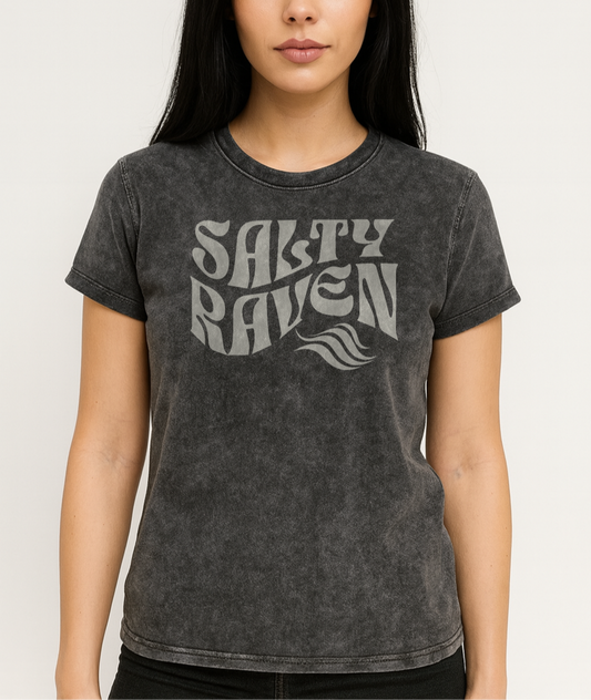 Raven model wears a unisex relaxed fit soft vintage black denim wash vintage graphic t-shirt with the slogan 'Salty Raven' in white retro 70s wavy font. Branded RedBlonde in red on inside neck and right sleeve