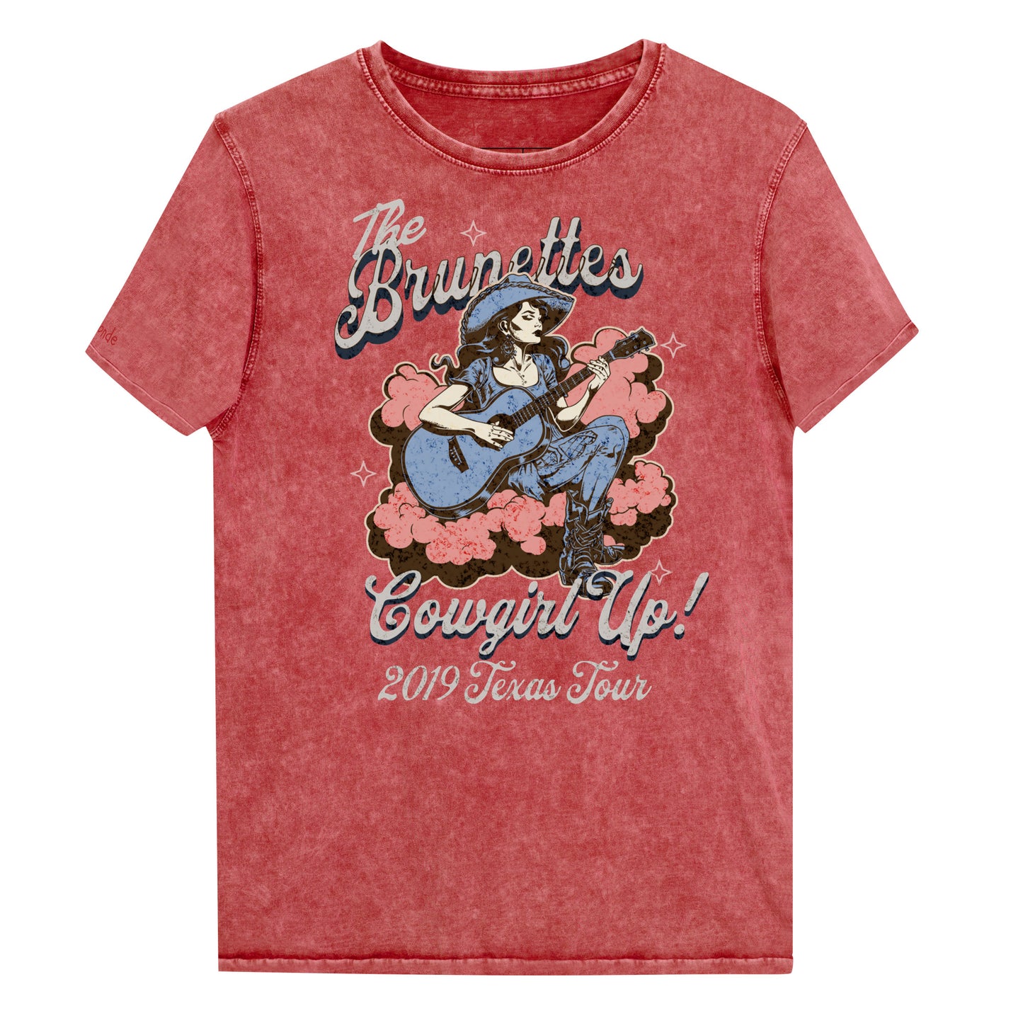 Red Garnet unisex t-shirt with a faded wash, featuring a retro graphic of a cowgirl playing a guitar surrounded by pink clouds. Text reads 'The Brunettes – Cowgirl Up! 2019 Texas Tour' in a Western-style font. Branded RedBlonde London on the inside neck and right sleeve