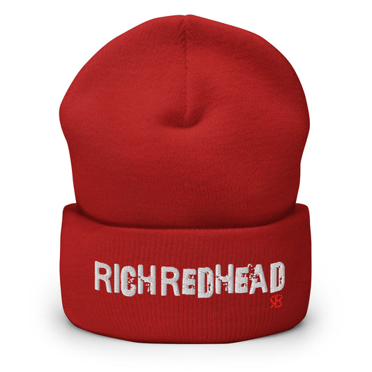Red cuffed beanie with the embroidered slogan “RICH REDHEAD” in bold white distressed-style lettering, featuring a small red “RB” RedBlonde logo on the right side of the fold. The beanie is shown upright against a clean white background.