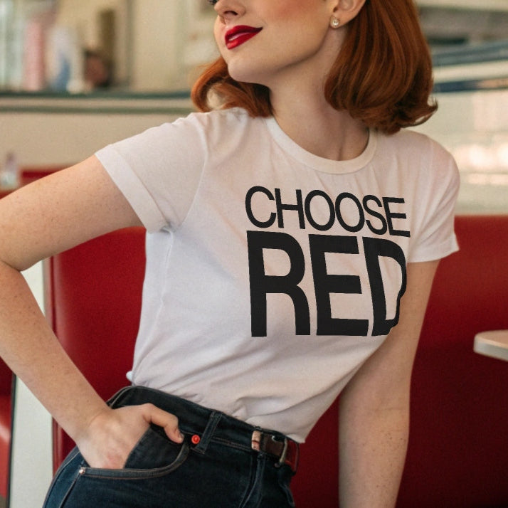 Redhead model in a 50s diner wears jeans and an 80s inspired white relaxed fit unisex t-shirt with the slogan ‘Choose Red’ in black helvetica now font.