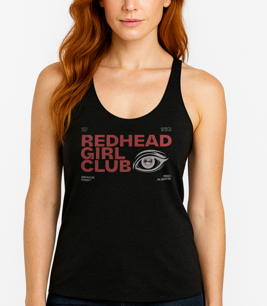 Redhead wears a Heather black women’s racerback tank top with bold red DT Getai Grotesh text reading “Redhead Girl Club” and a stylized black eye graphic to the right. Additional smaller text includes phrases like “Brains First,” “Blonde Always,” “Born to Be Bold,” and “ESTD 2025” arranged around the design.