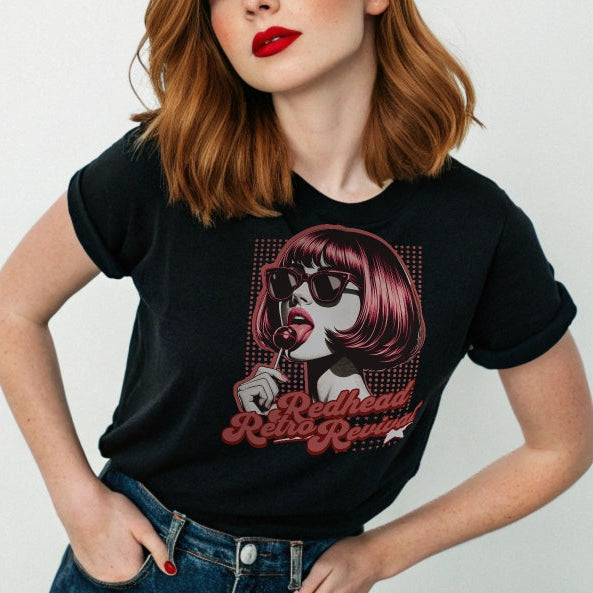 Redhead wears a black unisex t-shirt featuring a bold pop-art graphic of a stylish redheaded woman with a sleek bob haircut, red lips, and black sunglasses, holding a lollipop. The design includes red halftone dots and the retro-styled slogan "Redhead Retro Revival" in cursive typography with a star accent. RedBlonde branding appears on the inner neck label and red sleeve in red text.