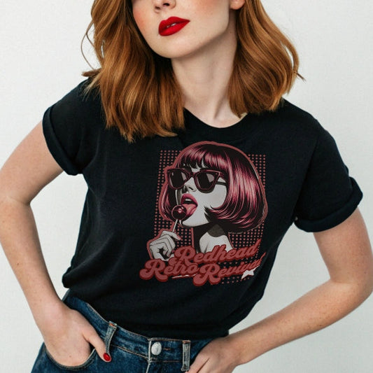 Redhead wears a black unisex t-shirt featuring a bold pop-art graphic of a stylish redheaded woman with a sleek bob haircut, red lips, and black sunglasses, holding a lollipop. The design includes red halftone dots and the retro-styled slogan "Redhead Retro Revival" in cursive typography with a star accent. RedBlonde branding appears on the inner neck label and red sleeve in red text.