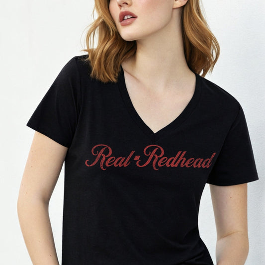Redhead wears a black women's relaxed fit v-neck slogan t-shirt with 'Real Redhead' in milkshake script red font. Branded RedBlonde in red on inside neck and right sleeve