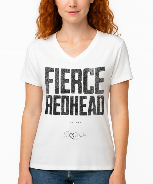 Redhead wears a white women’s V-neck T-shirt featuring the bold black distressed text “FIERCE REDHEAD” in large North Road capital letters across the chest. Beneath the text, the year “2025” is printed in small type, with the “RedBlonde” brand signature logo below it. The inner collar shows the “RedBlonde” brand name in red along with sizing and care details, and “RedBlonde” is also printed in small red letters on the right sleeve.