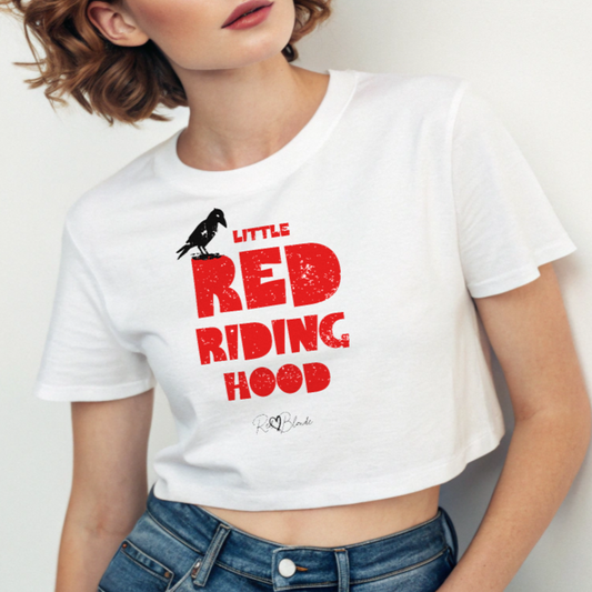 Redhead wears a white women’s crop top featuring bold distressed red Love Birds font reading “Little Red Riding Hood” with a small black crow perched on the word “Little,” and the RedBlonde signature logo below.