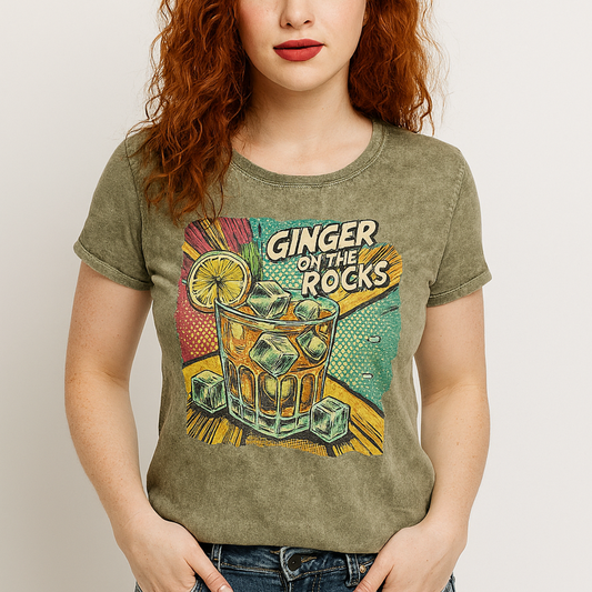 Redhead wears an army green acid-wash unisex denim look T-shirt featuring a vibrant, retro-style graphic of a cocktail glass filled with ice cubes, a lemon slice, and the text "GINGER ON THE ROCKS" in bold comic-style lettering. The background of the graphic includes colorful pop art elements in yellow, green, and turquoise tones. Branded RedBlonde on the inside neck and right sleeve