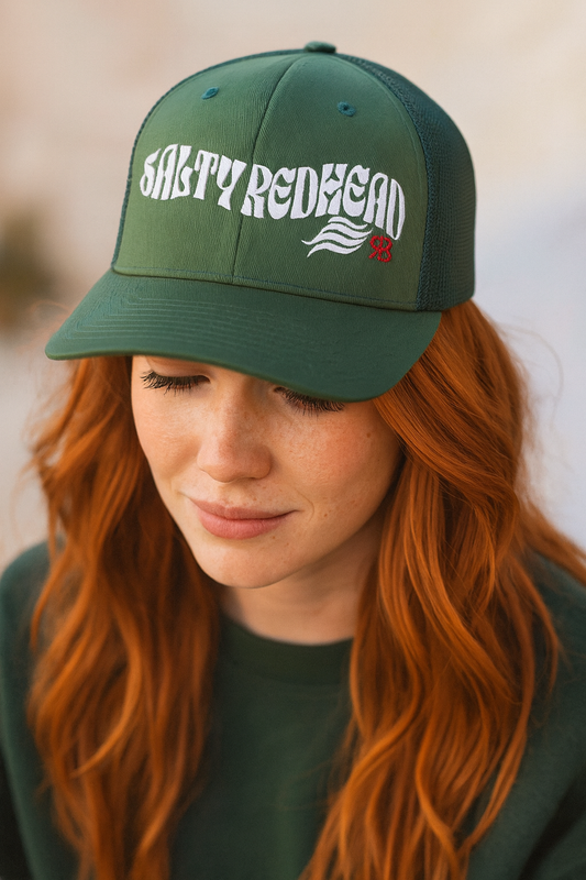 Redhead woman wearing a green trucker cap with 'Salty Redhead' in white Solino display font with RB logo in red