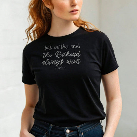 Redhead woman wears a black unisex t-shirt featuring the handwritten-style slogan “but in the end, the Redhead always wins” in Hillbear font in dark gray text across the chest, signed off RedBlonde. Branded “RedBlonde London on inside the collar and on the right sleeve