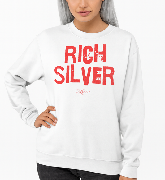 Silver haired model wears a white unisex premium sweatshirt with bold distressed red Ed Geinitext “RICH SILVER” on the front, featuring a subtle RedBlonde logo beneath the lettering and on the sleeve cuff and inside neck
