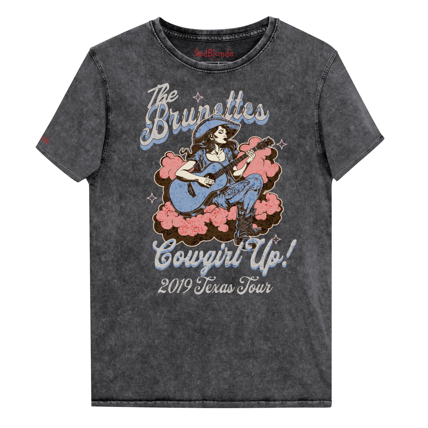 Vintage black unisex t-shirt with a faded wash, featuring a retro graphic of a cowgirl playing a guitar surrounded by pink clouds. Text reads 'The Brunettes – Cowgirl Up! 2019 Texas Tour' in a Western-style font. Branded RedBlonde London on the inside neck and right sleeve