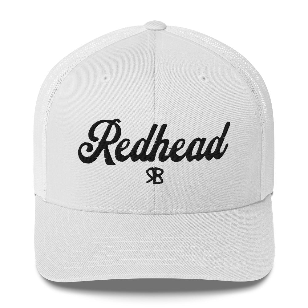 White trucker cap with 'Redhead' in black adventurer 01 font on front. Mesh back. Branded RB