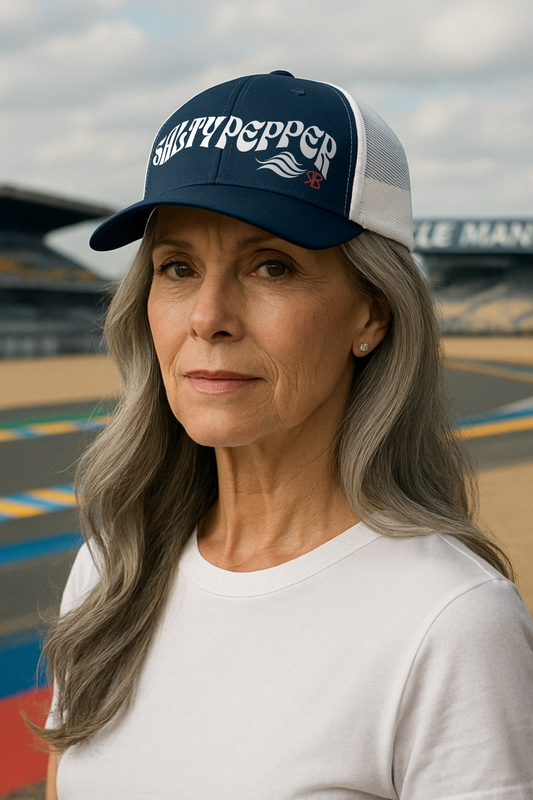 Woman wearing a navy/white trucker cap with 'SALTY PEPPER' in white Solino Display retro 70s wavy font standing in front of a race track. branded RedBlonde in red RB