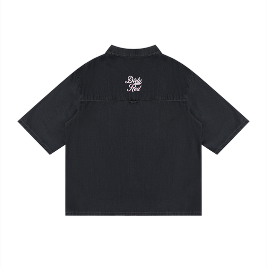 back view of a black, short-sleeve button-up shirt with a subtle faded finish and a small raised “Dirty Red” Milkstore script logo centered across the upper back.