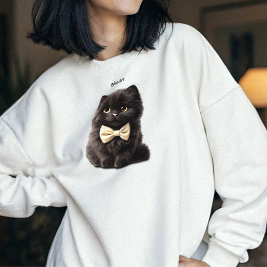 black haired model wears white relaxed fit unisex hoodie with a cute graphic of a Jet black kitten wearing a bow-tie and the words 'the Jet' linking to Black hair. Branded RedBlonde in red on inside neck and right cuff