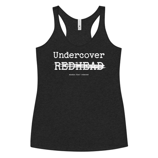 A black racerback tank featuring a bold white text reading “Undercover REDHEAD” with “REDHEAD” partially struck through by a horizontal white bar. Beneath it, smaller text says “mission file // redacted” along with a subtle RedBlonde logo. Branded RedBlonde London in red on the reverse