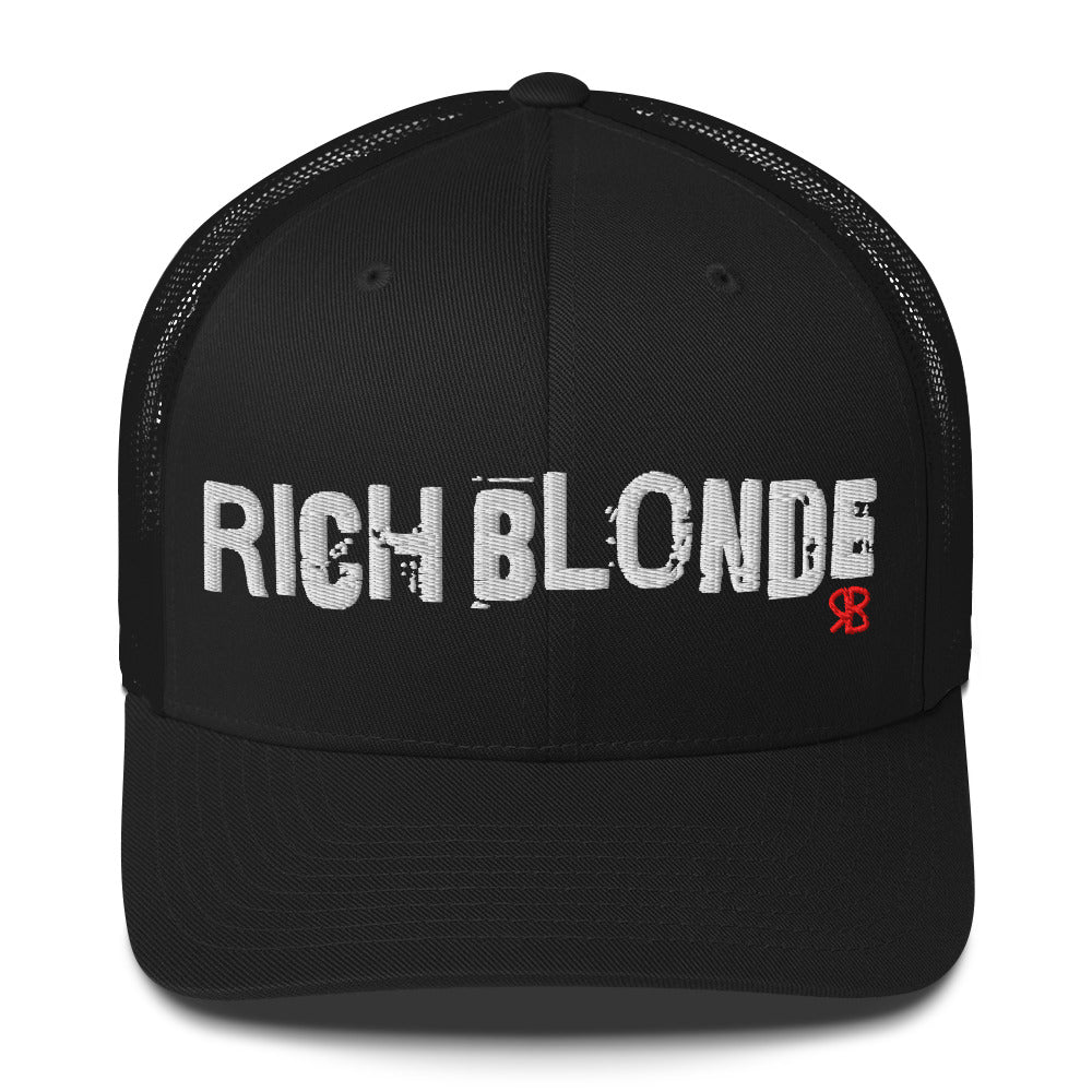 Black mesh-back trucker cap with the bold distressed text “RICH BLONDE” embroidered in white across the front, and a small red “RB” logo detail beneath the text. The cap has a structured front panel and curved brim