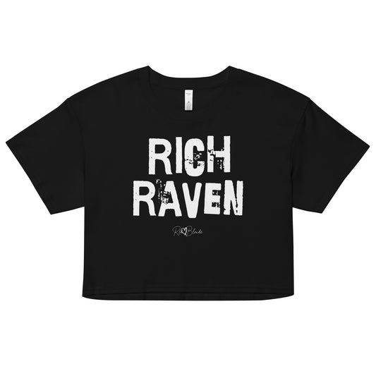 A black coloured crop top with a relaxed fit, short sleeves, and a wide crew neckline. The front features bold white distressed lettering reading “RICH RAVEN” with the RedBlonde signature logo underneath in white