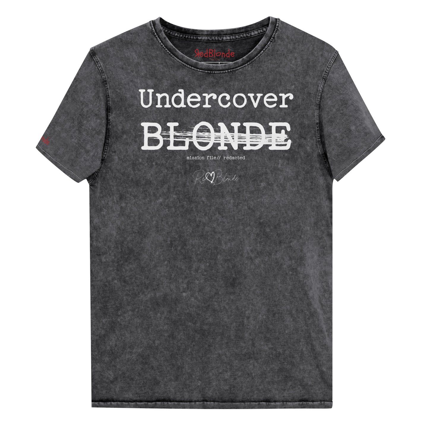 A black unisex denim-style t-shirt with a vintage washed finish. The front features bold white text reading “Undercover BLONDE” with “BLONDE” partially struck through by a horizontal white bar. Beneath it, smaller text says “mission file // redacted” along with a subtle RedBlonde logo. The shirt has a classic crew neck and short sleeves with visible stitching for a rugged look. Branded RedBlonde London in red on inside neck and right sleeve