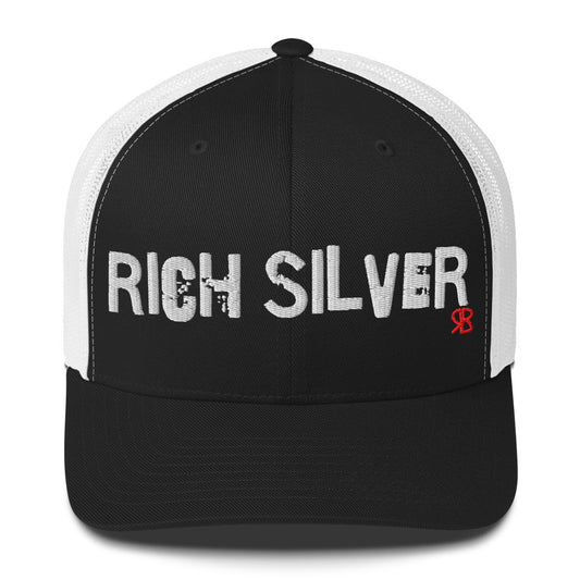 Black / white mesh-back trucker cap with the bold distressed text “RICH SILVER” embroidered in white across the front, and a small red “RB” logo detail beneath the text. The cap has a structured front panel and curved brim