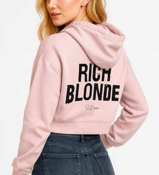 Back view of a Blonde wearing a cropped ice-wash pale pink hoodie with bold black “RICH BLONDE” Ed Gein font and the RedBlonde signature logo printed below.
