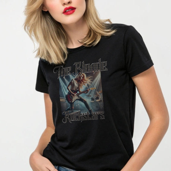 blonde wears a black unisex t-shirt with a graphic of a blonde female rock guitarist on stage with a drummer in the background, illuminated by stage lights. The text ‘The Blonde Rockstars’ is in bold, metallic avalen rekas font above and below the image. Branded RedBlonde London in red on the inside neck and right sleeve.