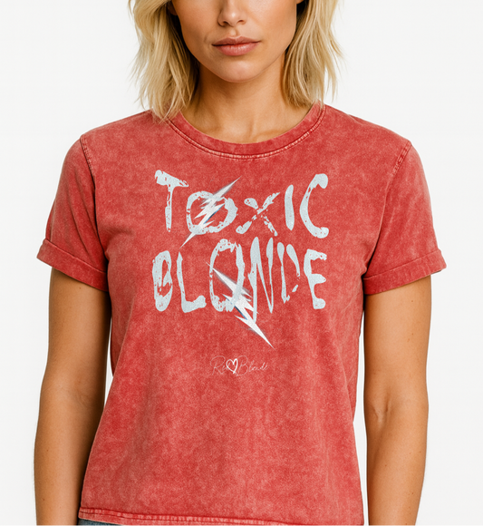 Blonde wears a Red Garnet acid-wash denim-style unisex t-shirt with the bold graphic text “TOXIC BLONDE” in distressed light blue Chainsaw Carnage lettering across the front, featuring the RedBlonde logo subtly printed below the text. Branded RedBlonde in red in inside neck and right sleeve