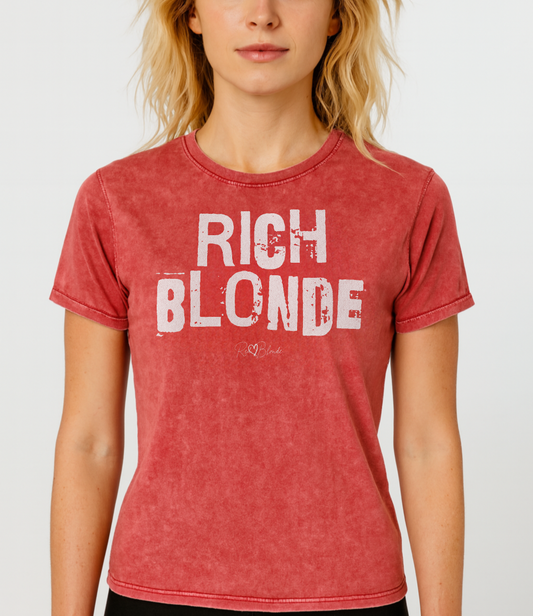 Blonde wears a red acid-wash unisex denim T-shirt with a distressed vintage look. The shirt features "RICH BLONDE" in bold white Ed Gein font with the RedBlonde signature logo underneath. The shirt has short sleeves, a crew neckline, and visible seam detailing for a rugged, casual style. Branded Redblonde on inside neck and right sleeve