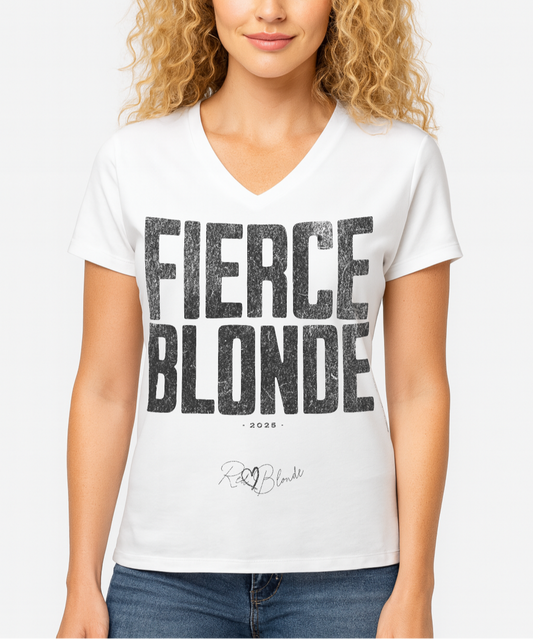 blonde wears a White women’s V-neck T-shirt featuring the bold black distressed text “FIERCE BLONDE” in large North Road capital letters across the chest. Beneath the text, the year “2025” is printed in small type, with the “RedBlonde” brand signature logo below it. The inner collar shows the “RedBlonde” brand name in red along with sizing and care details, and “RedBlonde” is also printed in small red letters on the right sleeve.