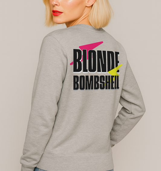 Blonde wears a Light grey unisex sweatshirt seen from the back with bold black Krisha text “BLONDE BOMBSHELL” accented by a pink lightning bolt through “BLONDE” and a yellow lightning bolt through “BOMBSHELL.”